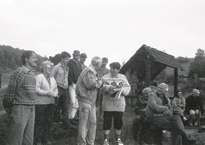 Black-and-white group photo featuring 10+ adults outdoors, likely mid-20th century (1960s–1970s). Central figures in casual a...