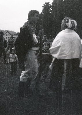 Vintage black-and-white photo of a rural outdoor gathering, likely a folk festival or harvest celebration. Central figures in...