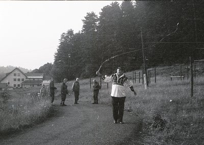 Black-and-white rural scene featuring a group of men playing frisbee on a grassy path, likely mid-20th century. Foreground ma...