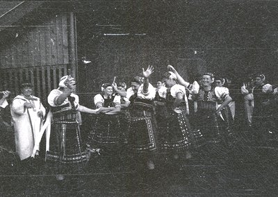 Traditional folk dance performance in intricate embroidered costumes, likely Eastern European. Women in layered skirts with f...