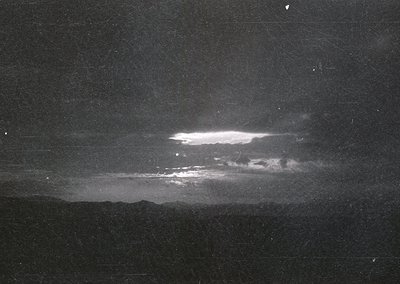 Vintage high-contrast black-and-white photograph of a dramatic nighttime sky with a bright, elongated aurora borealis display...