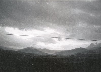 Vintage black-and-white landscape featuring low-hanging clouds over misty mountain ranges, with a horizontal power line cutti...