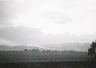 Vintage black-and-white landscape featuring rolling hills and sparse vegetation under overcast skies. Low-contrast monochrome...