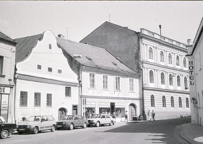 Mid-20th century European street scene featuring three-story buildings with classic European architecture: stepped gables, ar...