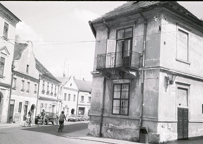 Mid-20th century European street scene featuring weathered two-story building with wrought-iron balcony and peeling plaster. ...