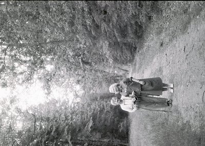 Two figures stand in a cavernous, sunlit rock formation, silhouetted against bright light. The vertical rock walls and natura...