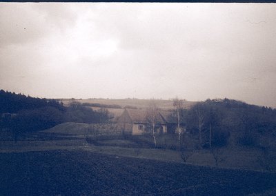 Vintage sepia-toned rural scene featuring a single-story farmhouse with a pitched roof, surrounded by open fields and leafles...