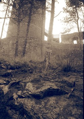 A sepia-toned photograph of a weathered, abandoned stone structure with a sign reading "TOCHIN" and "ПЕРЕСЕЛЕНИЕ" (meaning "r...