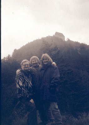 Vintage black-and-white photo of three adults posing on a misty hillside, with a medieval fortress ruin in background. Mid-20...