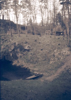 Vintage sepia-toned photo of a rugged, forested landscape with a rocky hillside and faintly visible wooden structure. Likely ...