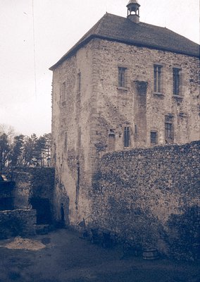Three-story stone fortress tower with crenellated roofline, flanked by high defensive walls. Small rectangular windows and a ...