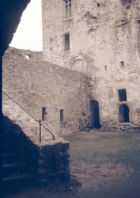 Historic stone courtyard with medieval architecture—weathered walls, arched doorways, and narrow windows. Likely Eastern Euro...