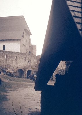 Medieval stone fortress courtyard with arched gatehouse and tower, framed by wooden beams. Likely Eastern European, 19th–earl...