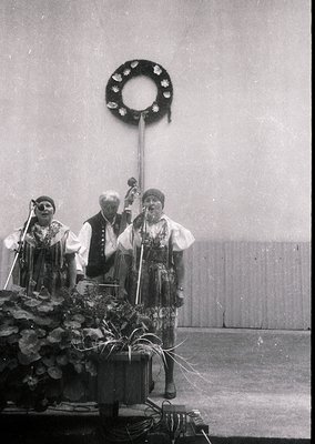 Black-and-white photo of three musicians in traditional folk attire performing on stage, likely Eastern European (1960s–1970s...