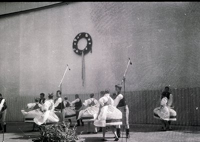 Black-and-white stage performance featuring women in traditional folk costumes, likely Eastern European, performing a circula...