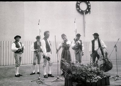 Traditional folk ensemble performing outdoors, likely Eastern European . Five musicians in folk attire—fiddles, accordion, fl...