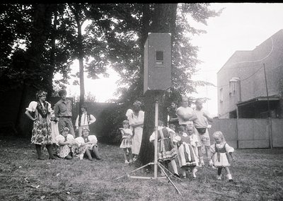 Vintage black-and-white photo of a mid-20th century outdoor gathering, likely 1950s–1960s. Group of adults and children pose ...