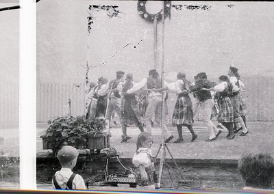 Vintage black-and-white photo of a group dance in an outdoor setting, likely early-to-mid 20th century. Participants in coord...