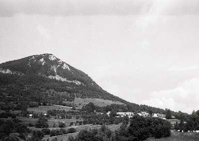 Mid-20th century black-and-white landscape featuring a steep, rocky mountain peak dominating the background. Foreground shows...
