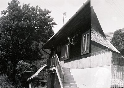 Mid-20th century wooden house with steep gable roof and decorative trim, set in a forested area. Exterior stairs lead to an e...