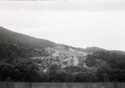 Black-and-white landscape featuring a rocky, terraced hillside with sparse vegetation, likely post-industrial or agricultural...