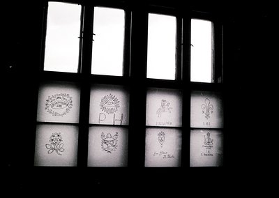 Vintage stained-glass window featuring intricate heraldic designs: fleur-de-lis, crowns, and floral motifs. Likely European, ...