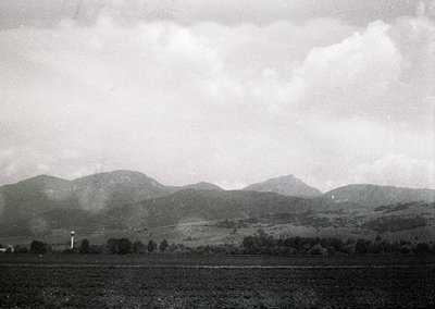 Vintage black-and-white landscape of rolling hills and farmland under overcast skies. Distant radio tower and sparse trees ma...