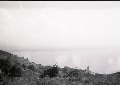 Vintage black-and-white coastal landscape with misty horizon and distant church spire. Rolling hills frame a serene seaside v...