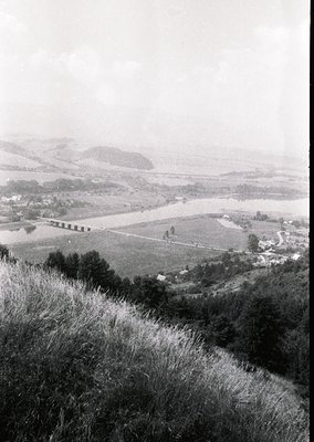 Mid-20th century black-and-white landscape featuring a winding river valley with agricultural fields, dense forest patches, a...