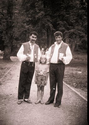Family portrait in traditional folk attire, mid-20th century. Two men in embroidered vests and knee-high boots flank a young ...