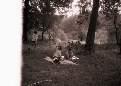 Vintage sepia-toned outdoor scene featuring a group of people lounging on a blanket in a wooded area, likely mid-20th century...