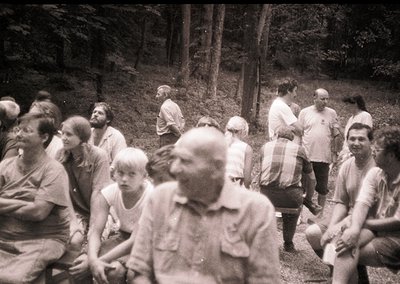 Group of people in a wooded area, likely mid-20th century. Casual summer attire suggests leisure or outdoor gathering. Dense ...