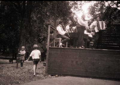 Vintage black-and-white photo of a folk band performing outdoors on a wooden platform, likely Eastern European . Accordionist...