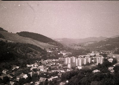 Vintage aerial view of a hilly town with mid-century concrete apartment blocks and clustered low-rise buildings. Lush greener...