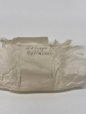 Wrinkled, aged paper envelope with handwritten text: *"Erlanger 95" / "Wollwaren"* (Wool goods). Likely 19th–early 20th centu...