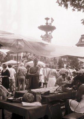 Vintage outdoor market scene featuring a bustling crowd around handcrafted food stalls. Ornate fountain with intricate ironwo...