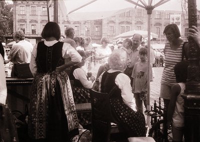 Vintage black-and-white street scene featuring a lively outdoor gathering, likely a folk festival or market. Women in traditi...
