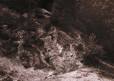 Monochrome close-up of ancient rock carvings depicting a seated figure, likely a historical or mythological depiction. The in...