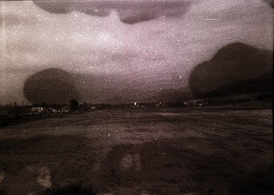 Vintage sepia-toned aerial view of a rural landscape with dense cloud cover. Low-lying fields and scattered buildings suggest...