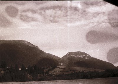 Vintage black-and-white alpine landscape with dramatic cloud formations over jagged peaks. Rolling meadows and sparse forest ...