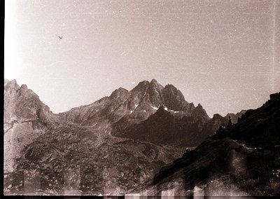Vintage sepia-toned alpine landscape with jagged peaks and rocky terrain, likely from mid-20th century. Single solitary figur...