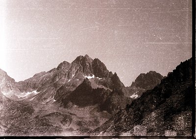 Vintage sepia-toned alpine peak with jagged ridges and snow patches, likely European Alps. Early 20th-century photographic gr...