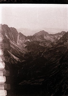 Vintage sepia-toned aerial view of rugged alpine terrain with steep ridges and scattered snow patches. Dramatic rock formatio...