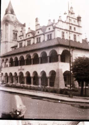 Vintage black-and-white photo of a grand European-style building with arched colonnade on ground floor, steep gabled roofs, a...