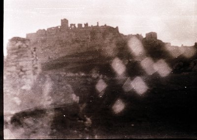 Vintage sepia-toned photo of a hilltop fortress with crumbling stone walls and towers, likely Eastern European. Fog obscures ...