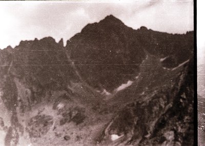 Vintage black-and-white aerial shot of rugged, snow-capped mountain terrain with jagged peaks and rocky slopes. Likely captur...