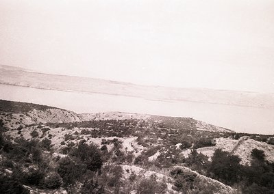 Vintage black-and-white landscape showing rugged, snow-dusted terrain with sparse vegetation. Rolling hills and distant horiz...