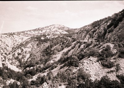 Black-and-white mountain landscape with rugged terrain and sparse vegetation, likely captured mid-20th century. Snow patches ...
