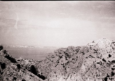 Vintage black-and-white coastal landscape featuring rugged cliffs and a calm sea horizon. The rocky terrain suggests a Medite...