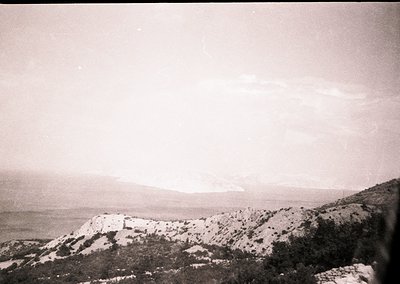 Vintage black-and-white seascape featuring rugged coastline with rocky cliffs and sparse vegetation. Distant shoreline meets ...